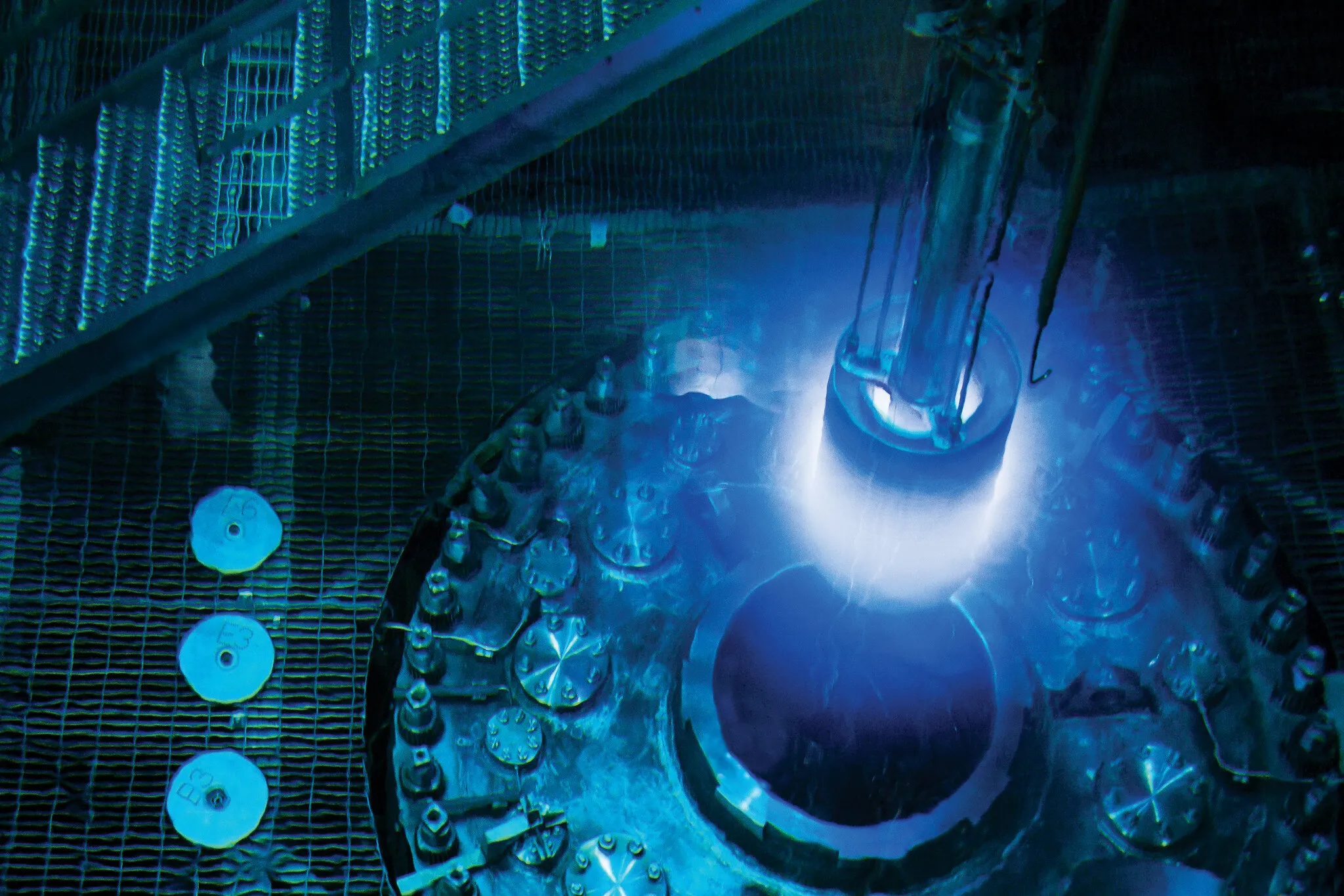 Blue Cherenkov light rises from an open reactor vessel as a fuel handling tool is lowered through the shielding water.